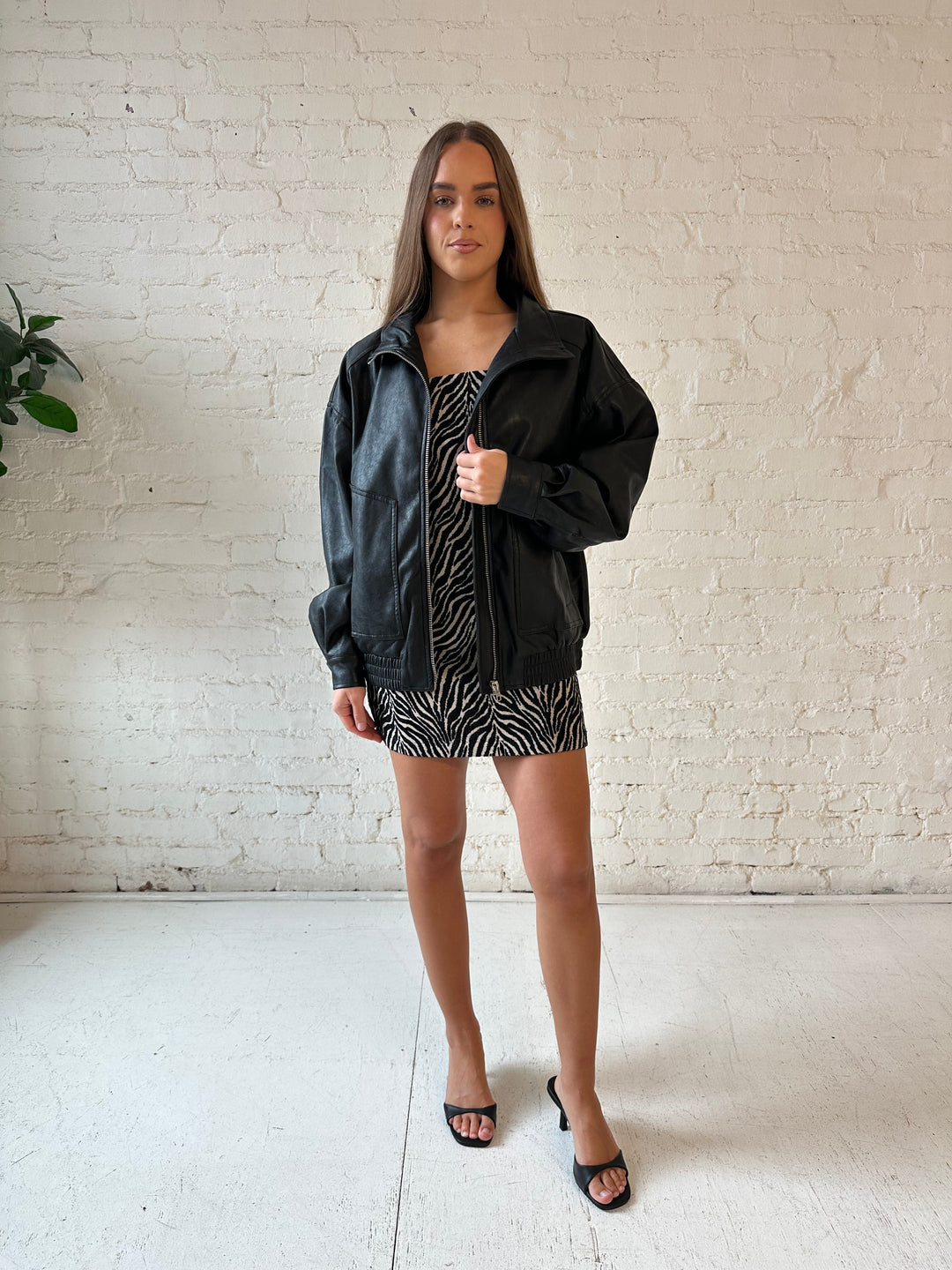 Woman wearing oversized black faux leather jacket with animal print mini dress.