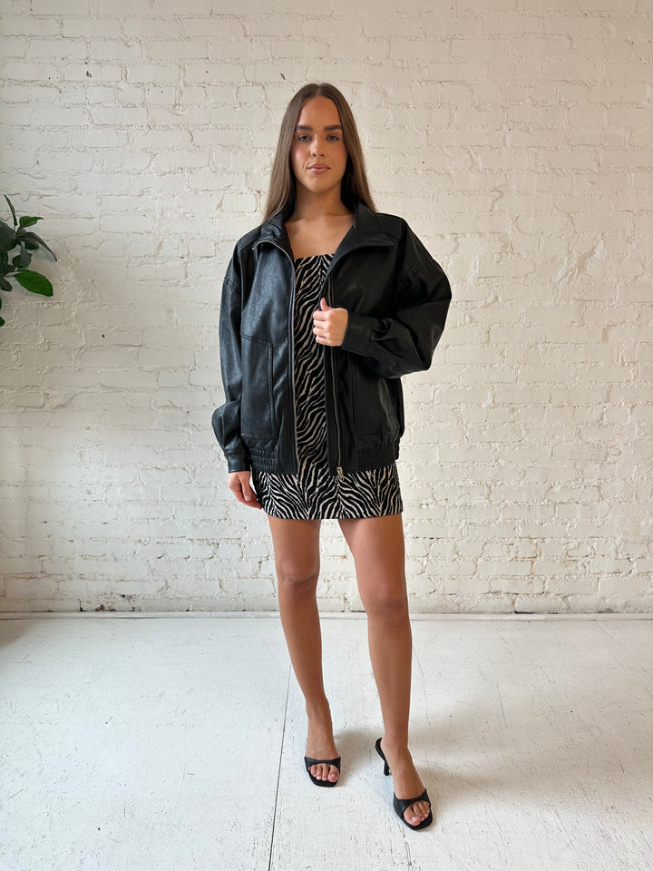 Woman wearing oversized black faux leather jacket with animal print mini dress.