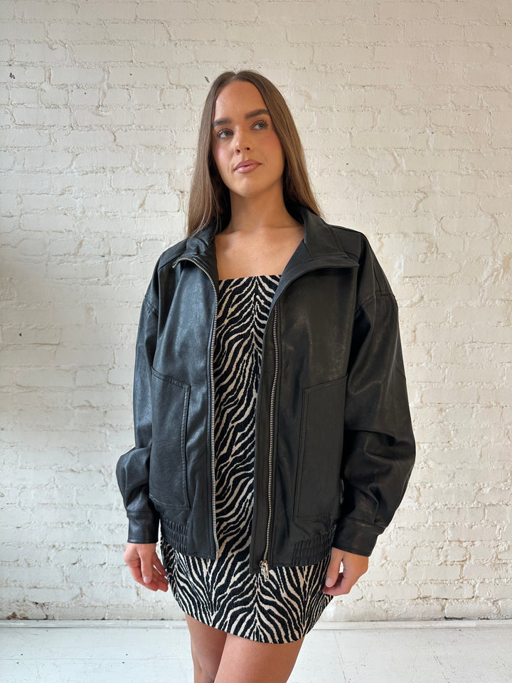 Woman wearing oversized black faux leather jacket with animal print mini dress.