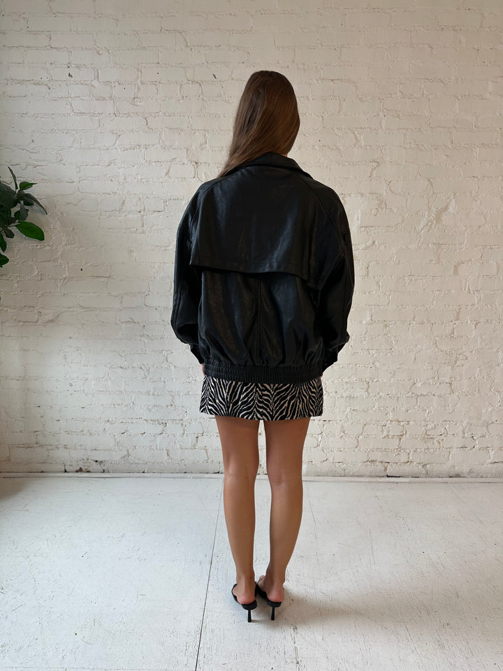 Woman wearing oversized black faux leather jacket with animal print mini dress.