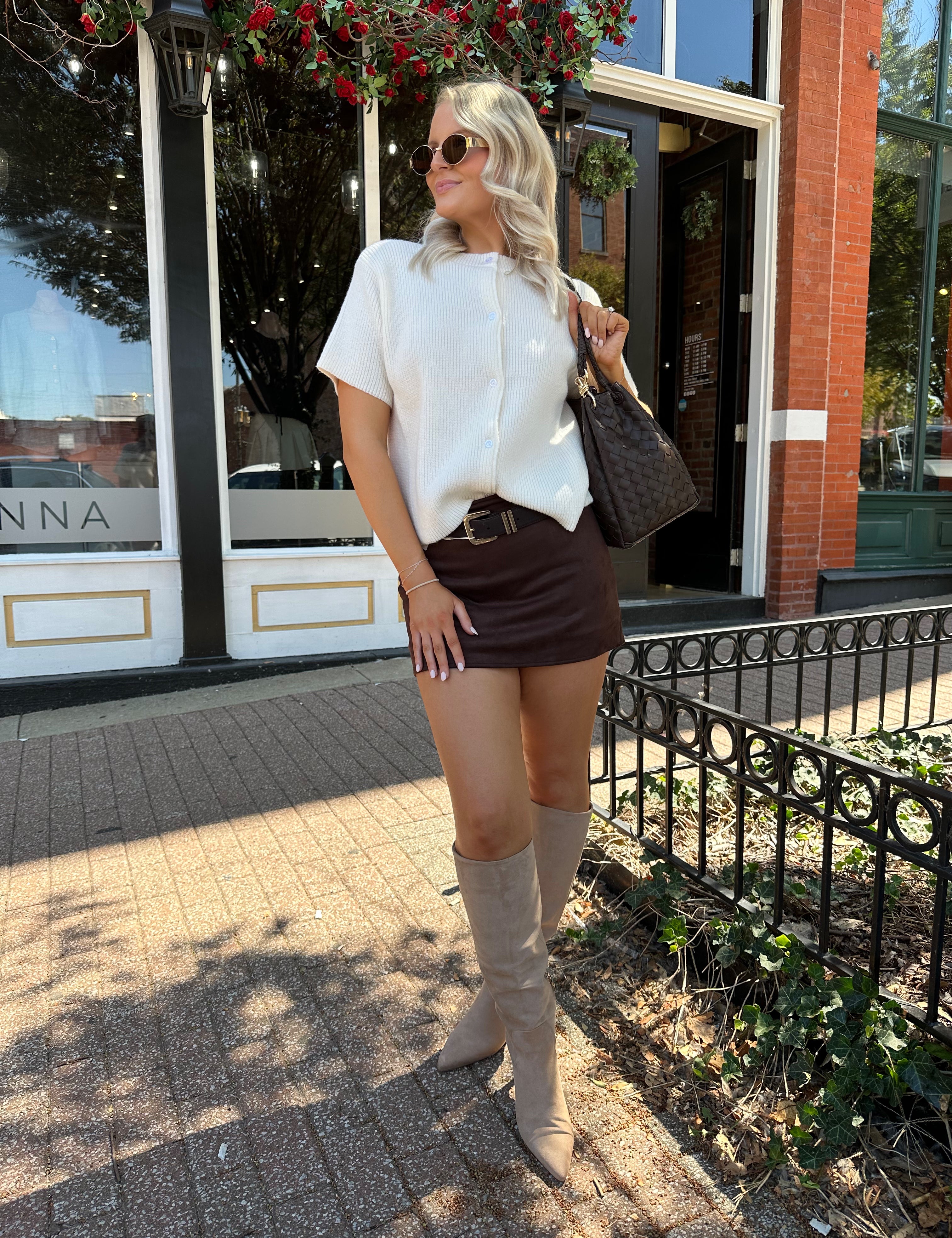 Woman wearing cream knit button up short sleeve top and brown suede skirt. 