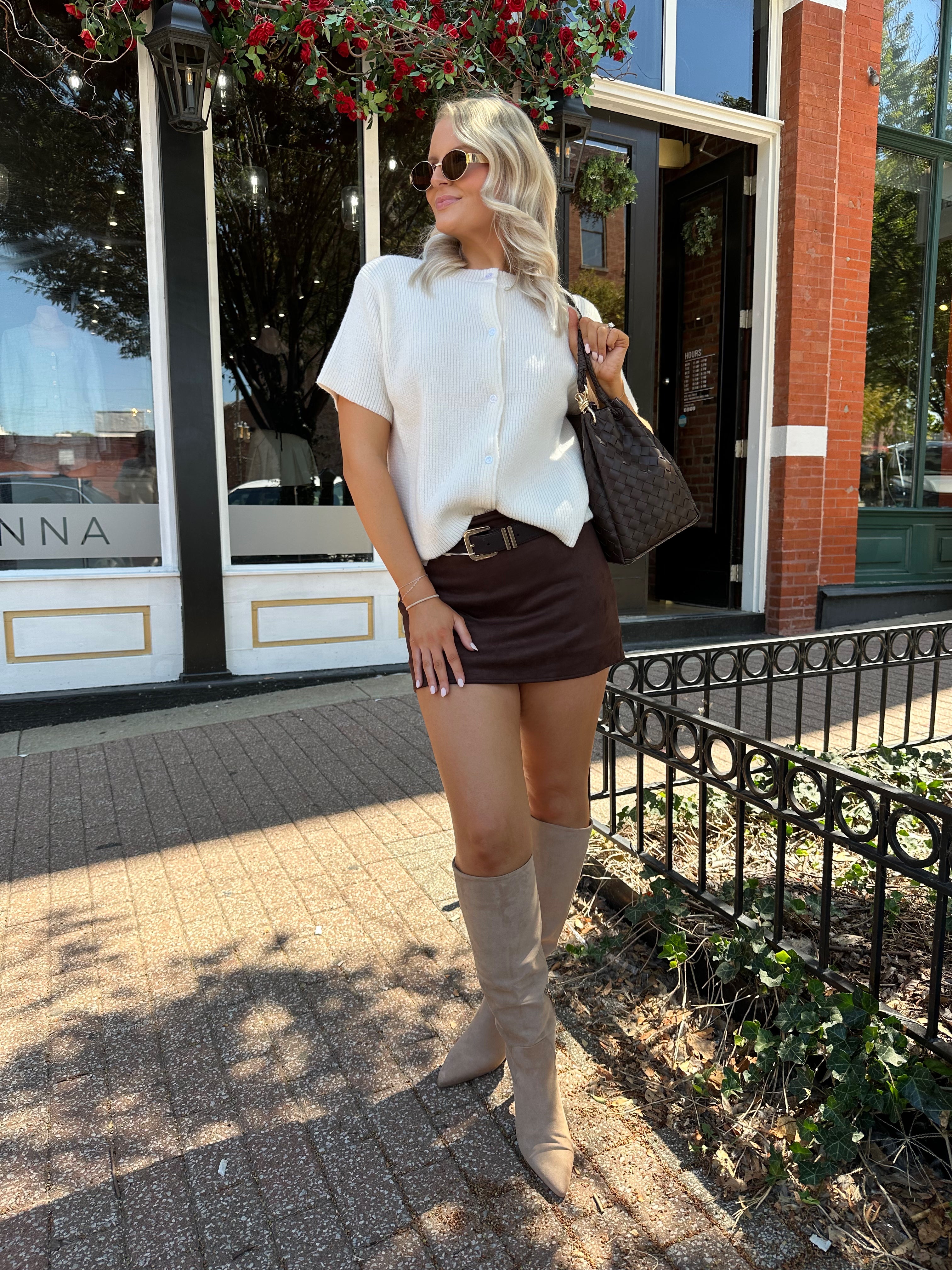 Woman wearing cream knit button up short sleeve top and brown suede skirt. 