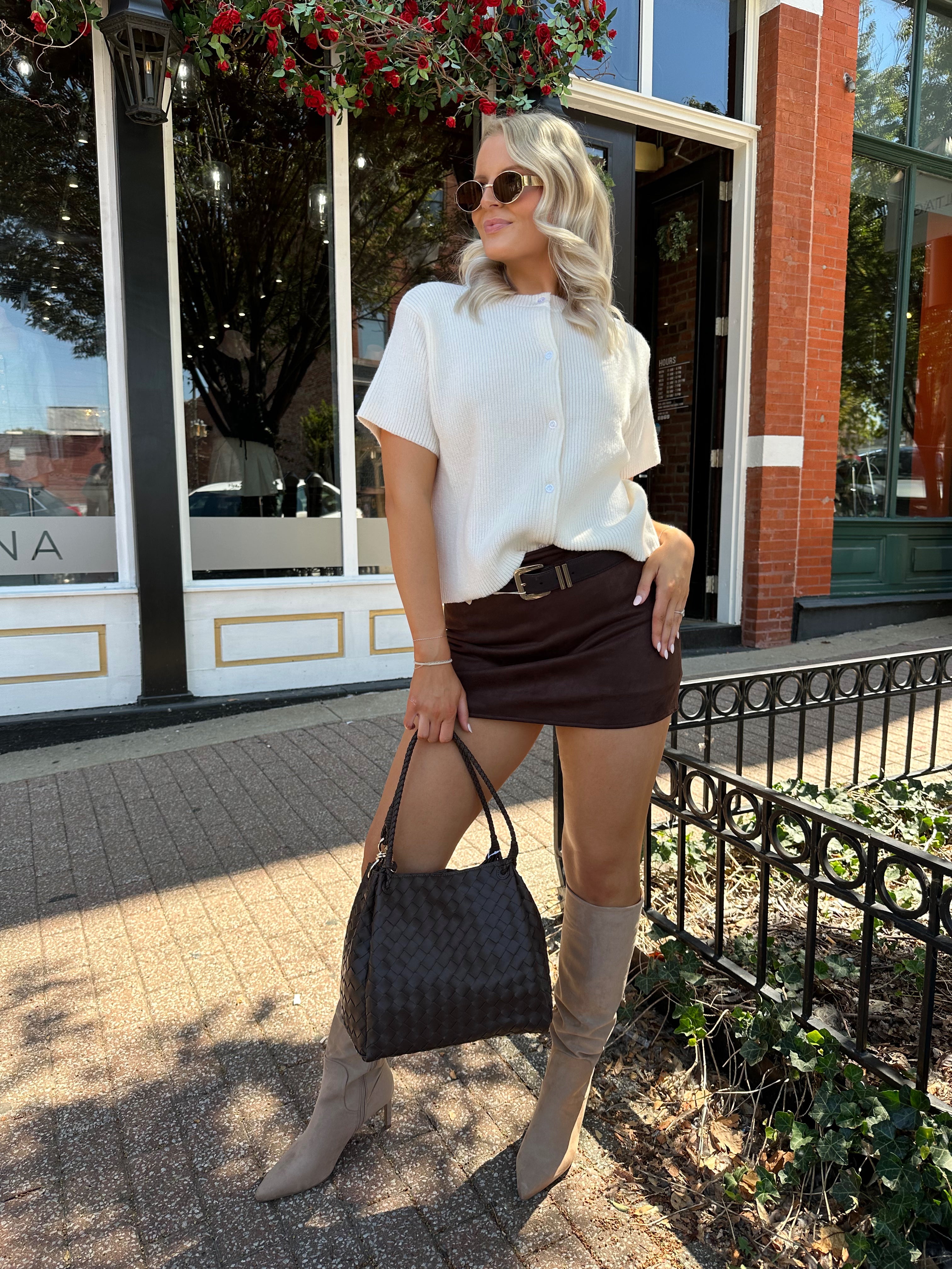 Woman wearing cream knit button up short sleeve top and brown suede skirt. 