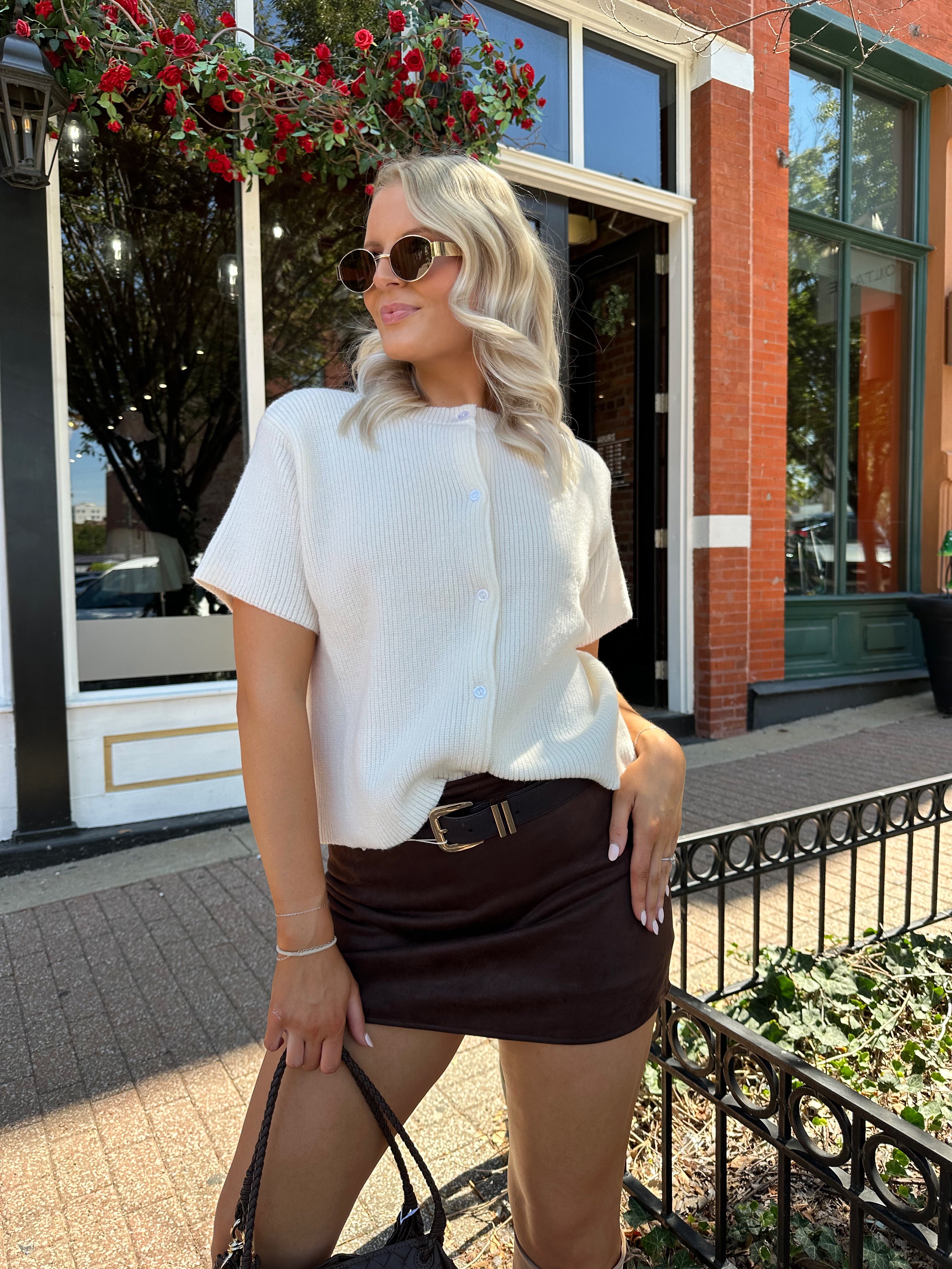 Woman wearing cream knit button up short sleeve top and brown suede skirt. 