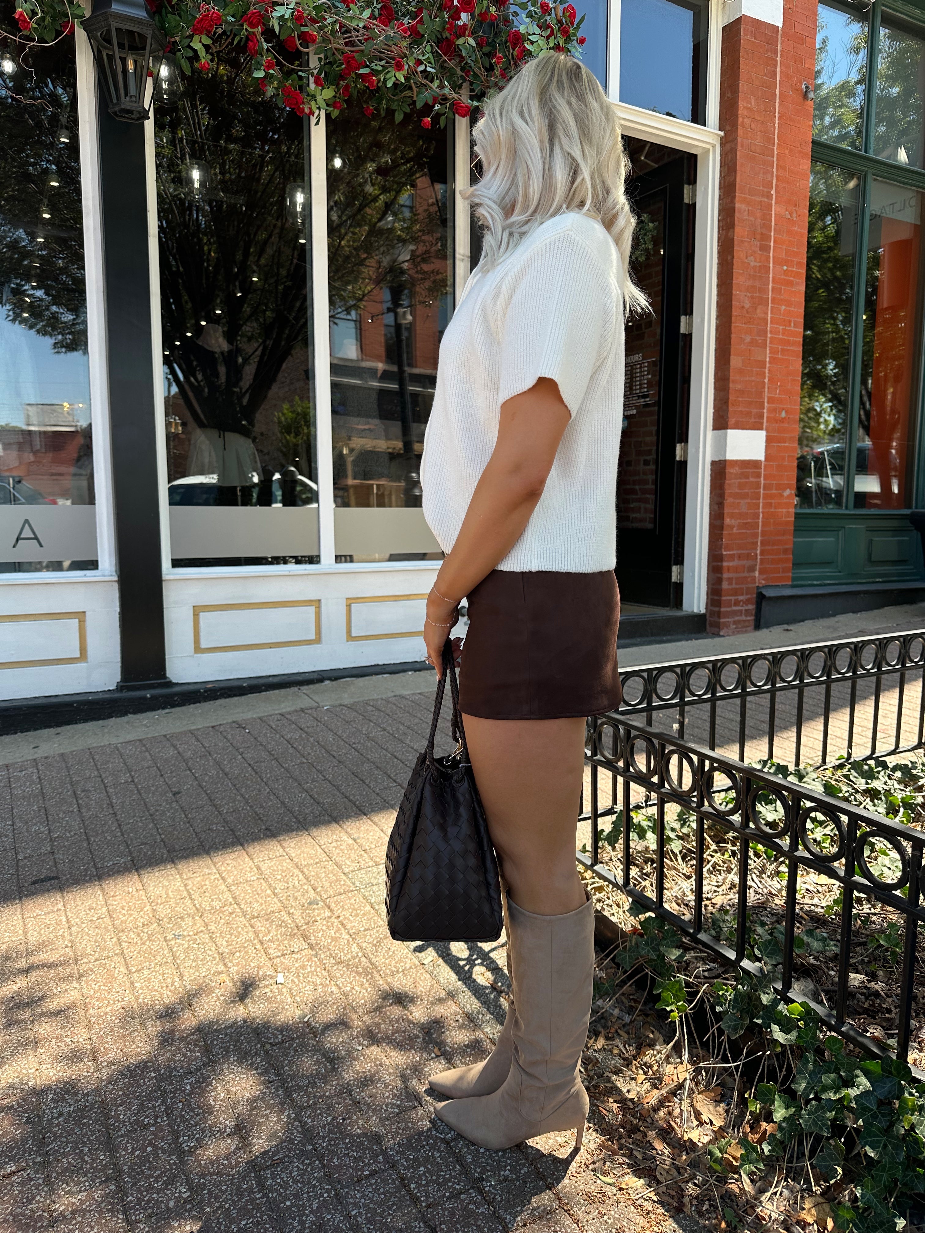Woman wearing cream knit button up short sleeve top and brown suede skirt. 