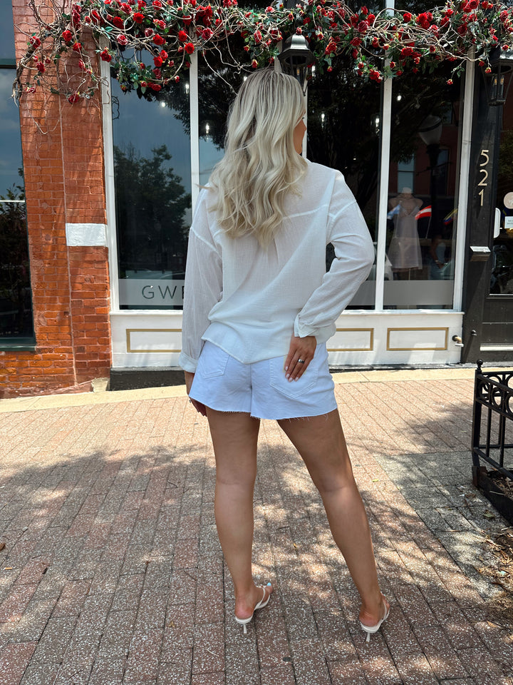 Woman wearing white button down top and white denim shorts.