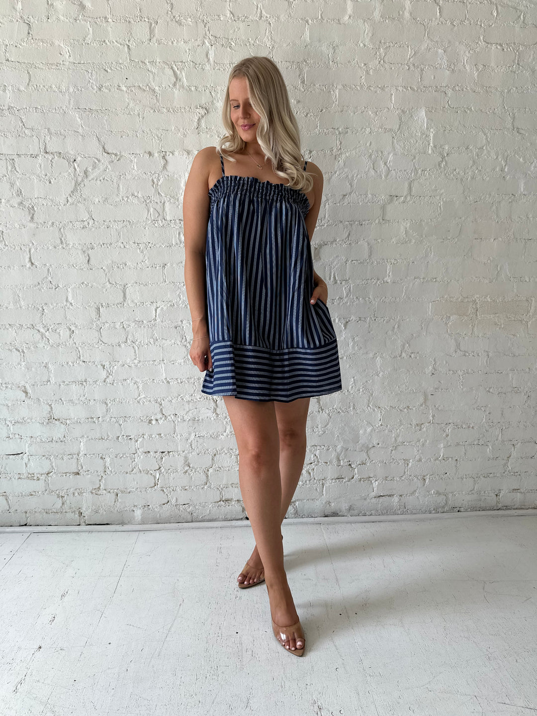 Woman wearing navy blue striped shift style mini dress with smocked neckline. 