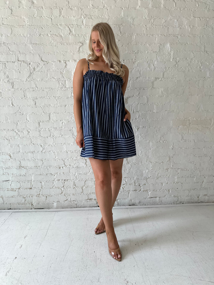 Woman wearing navy blue striped shift style mini dress with smocked neckline. 