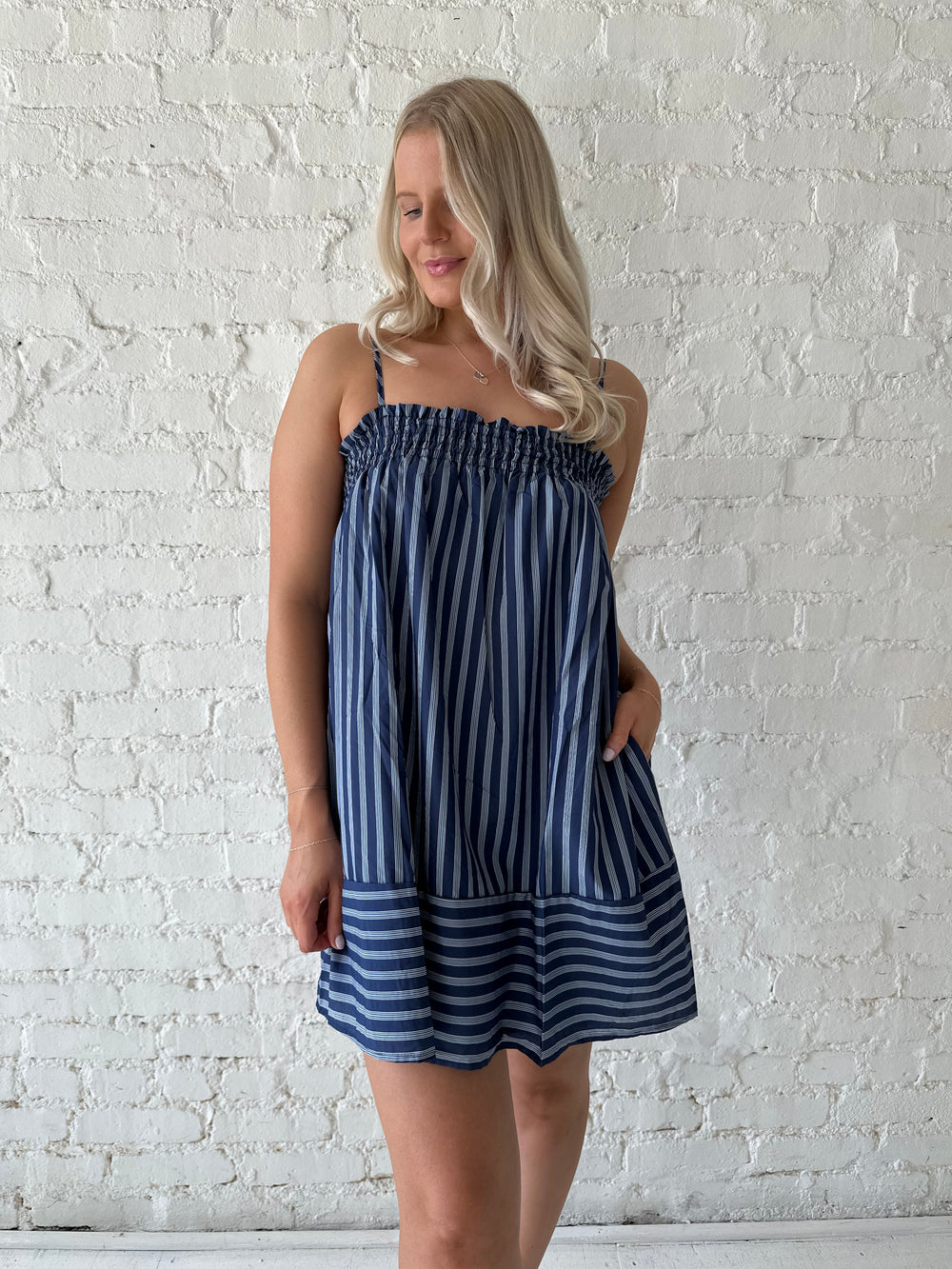 Woman wearing navy blue striped shift style mini dress with smocked neckline. 