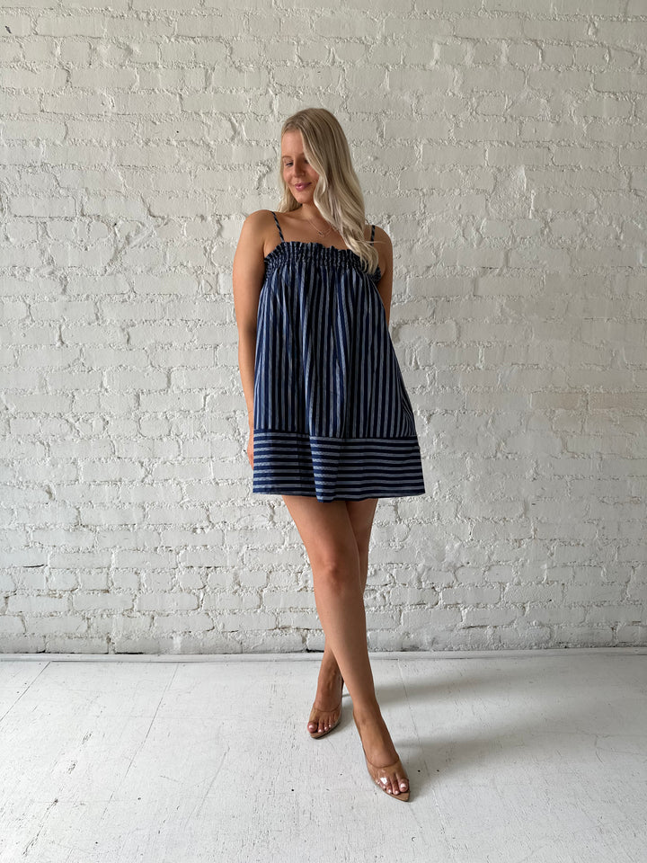 Woman wearing navy blue striped shift style mini dress with smocked neckline. 