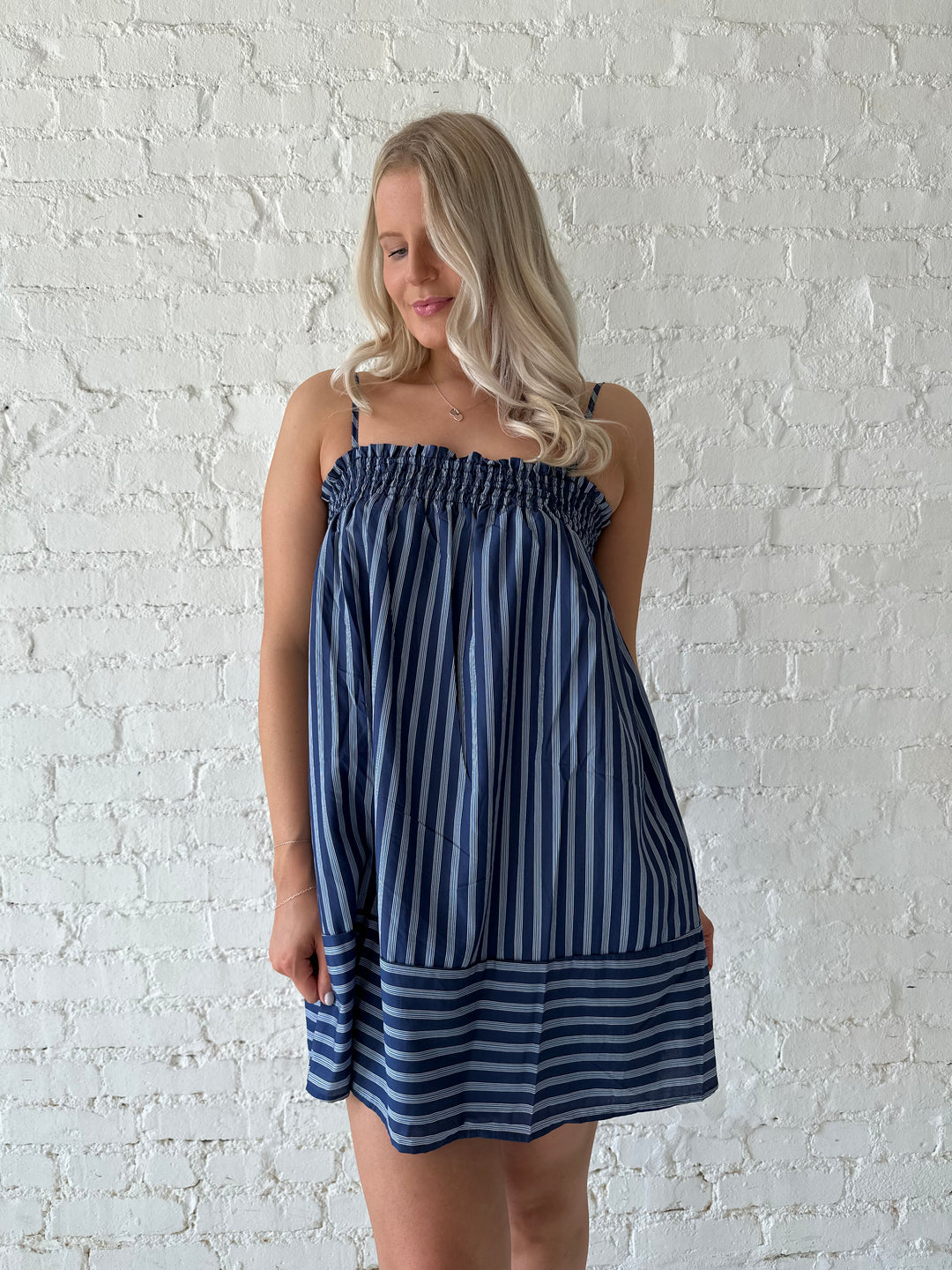 Woman wearing navy blue striped shift style mini dress with smocked neckline. 