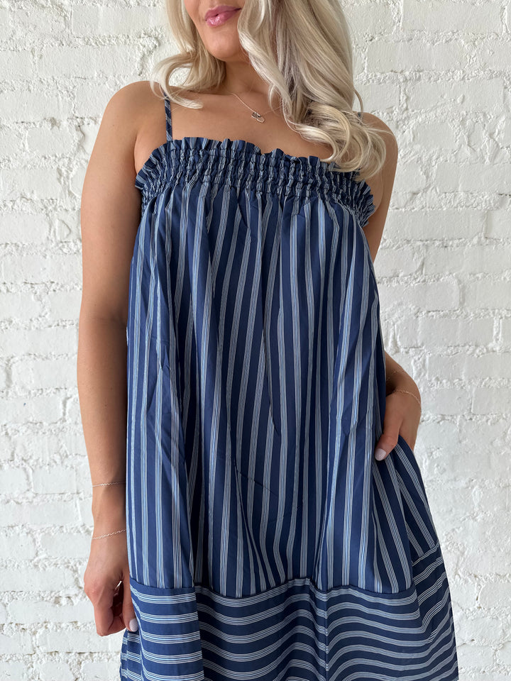 Woman wearing navy blue striped shift style mini dress with smocked neckline. 