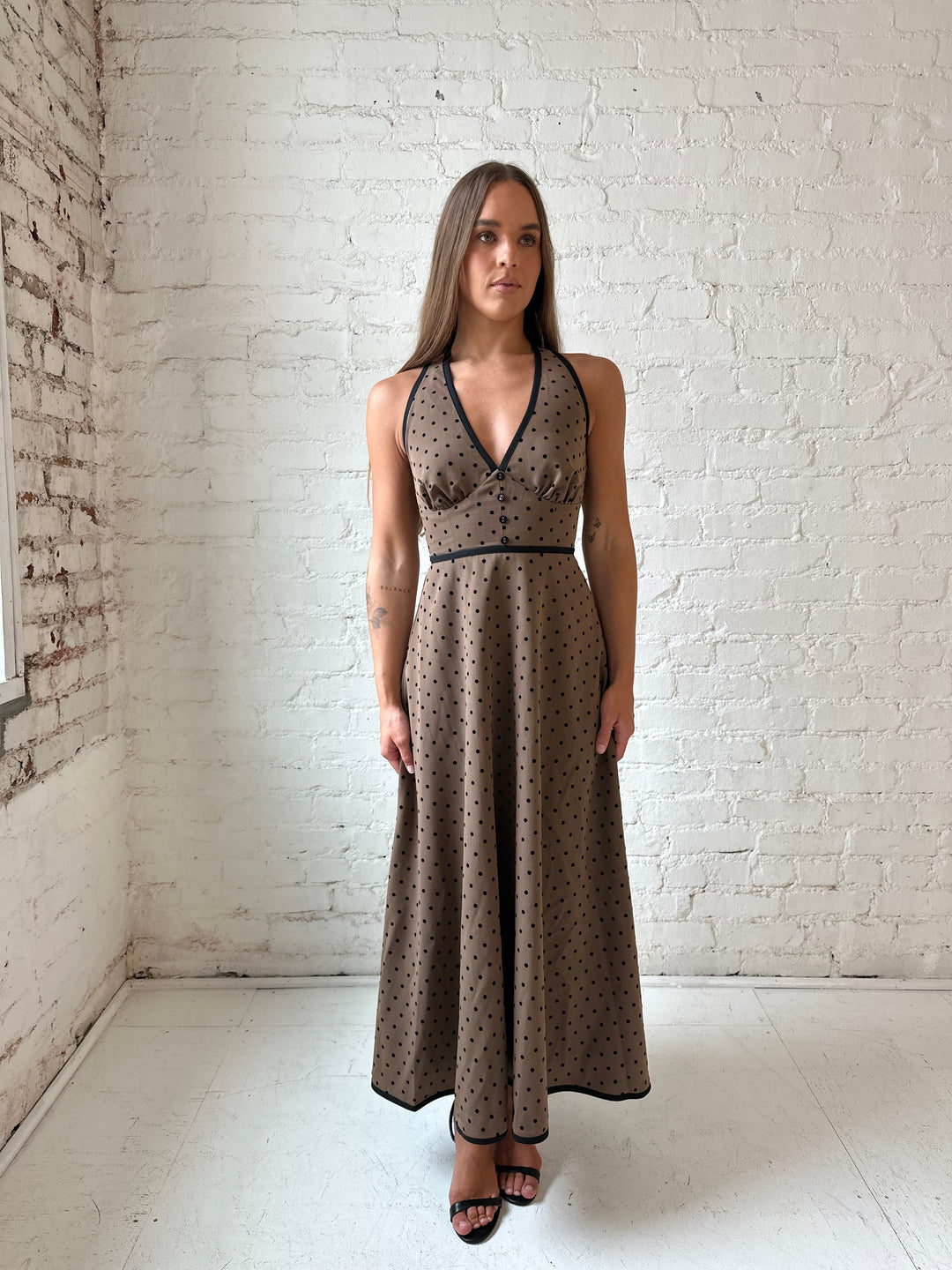 Woman wearing brown and black polka dot halter midi dress with a fit to flare style.