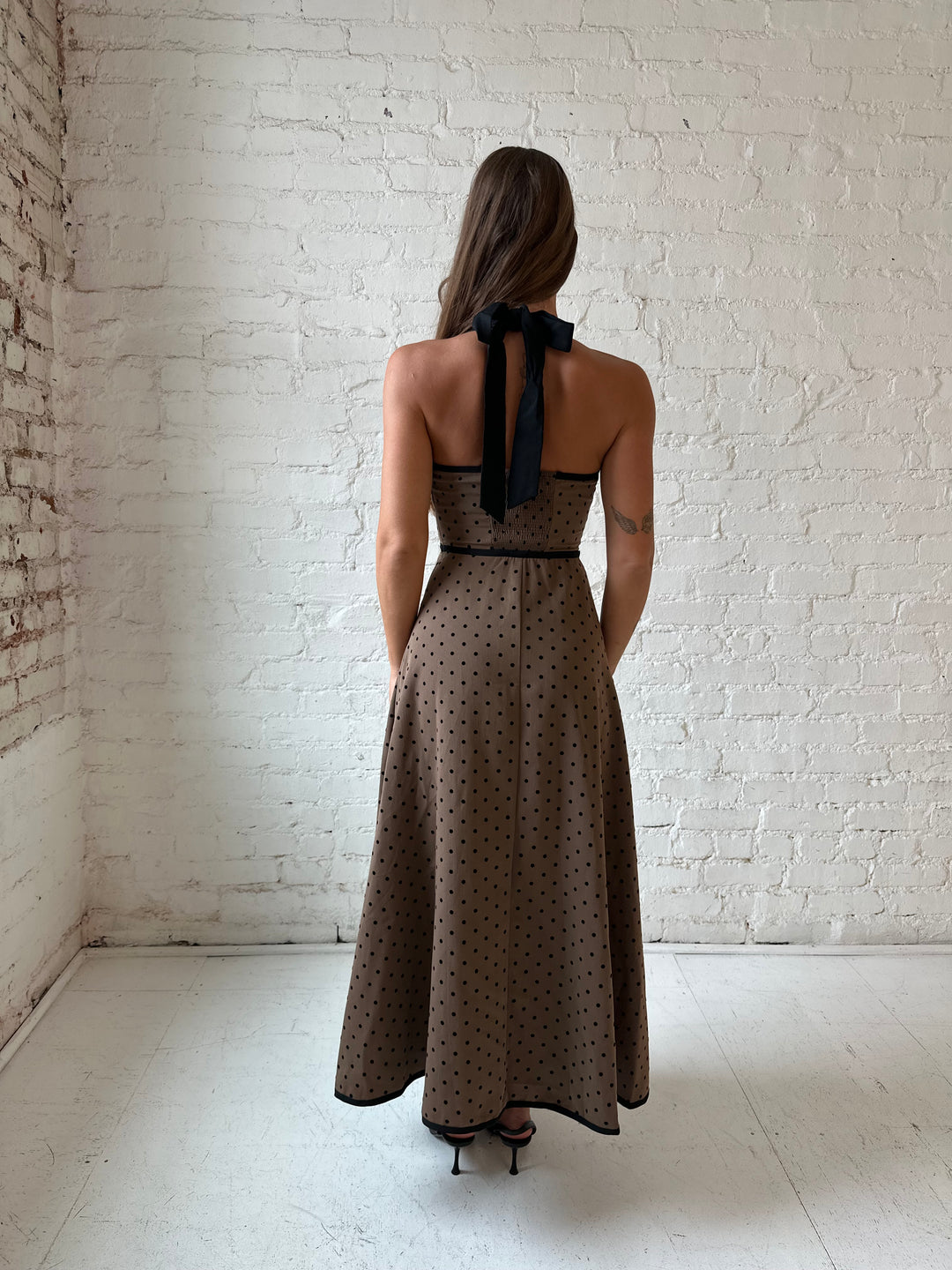 Woman wearing brown and black polka dot halter midi dress with a fit to flare style.