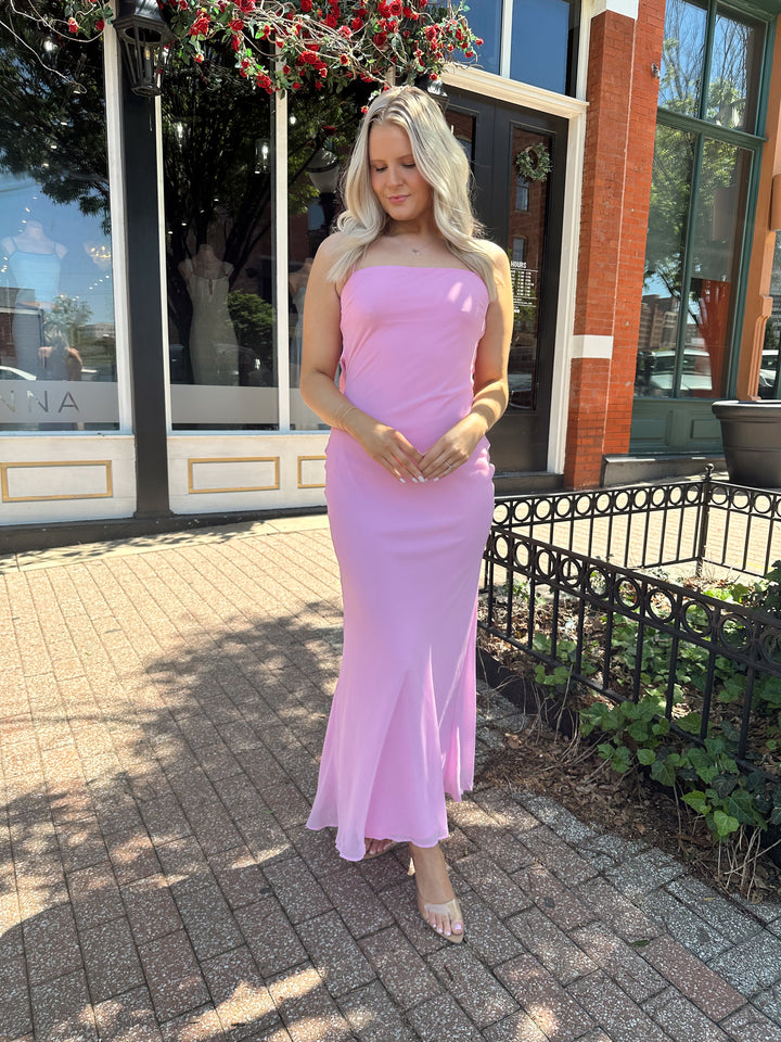 Woman wearing bright pink maxi dress with lace up back, and cowl back. 
