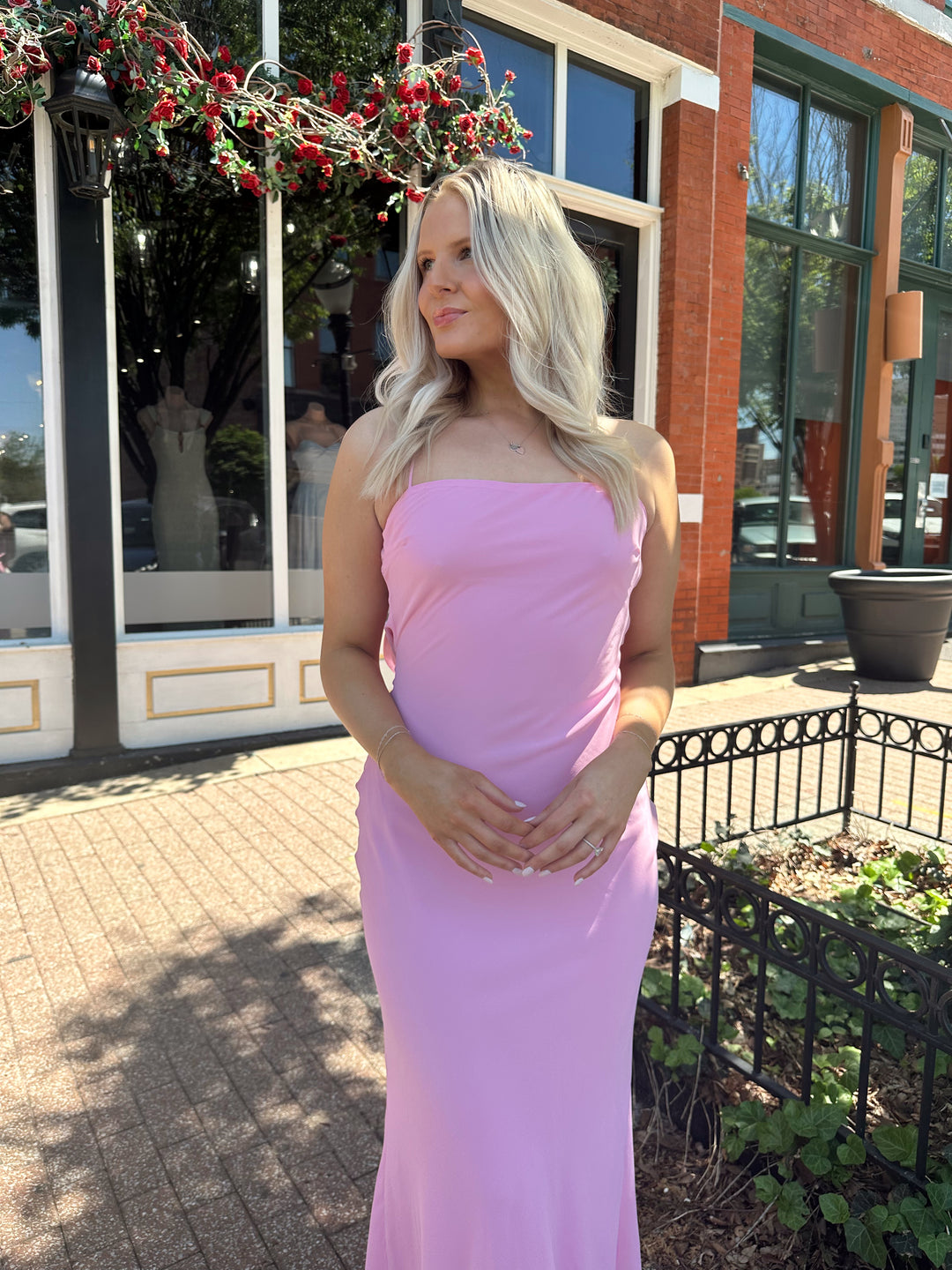Woman wearing bright pink maxi dress with lace up back, and cowl back. 