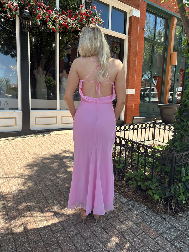 Woman wearing bright pink maxi dress with lace up back, and cowl back. 