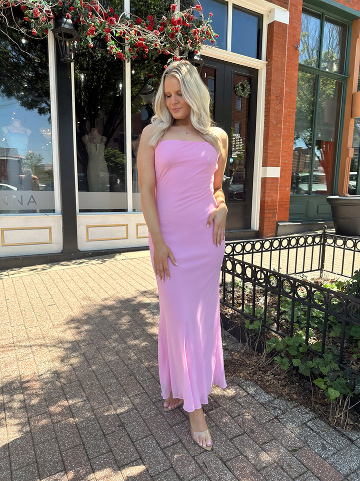 Woman wearing bright pink maxi dress with lace up back, and cowl back. 