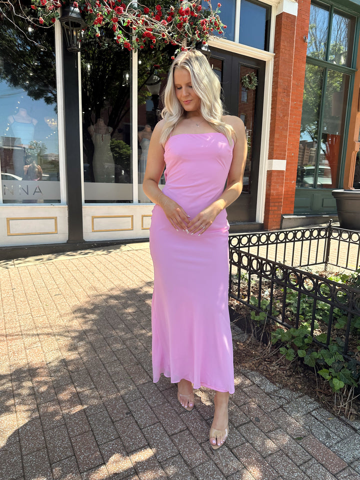 Woman wearing bright pink maxi dress with lace up back, and cowl back. 
