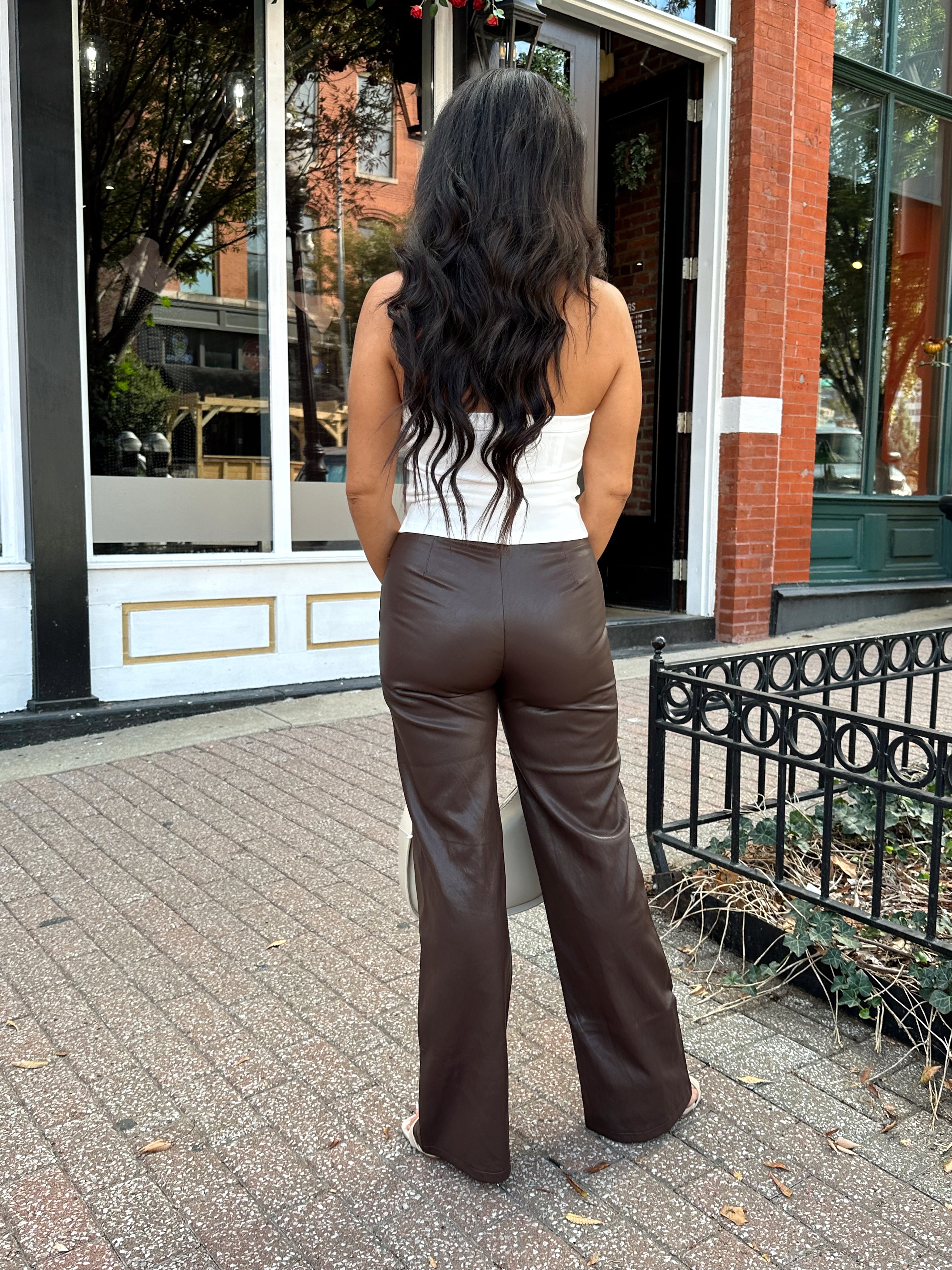 Woman wearing dark brown leather pants with tan top.