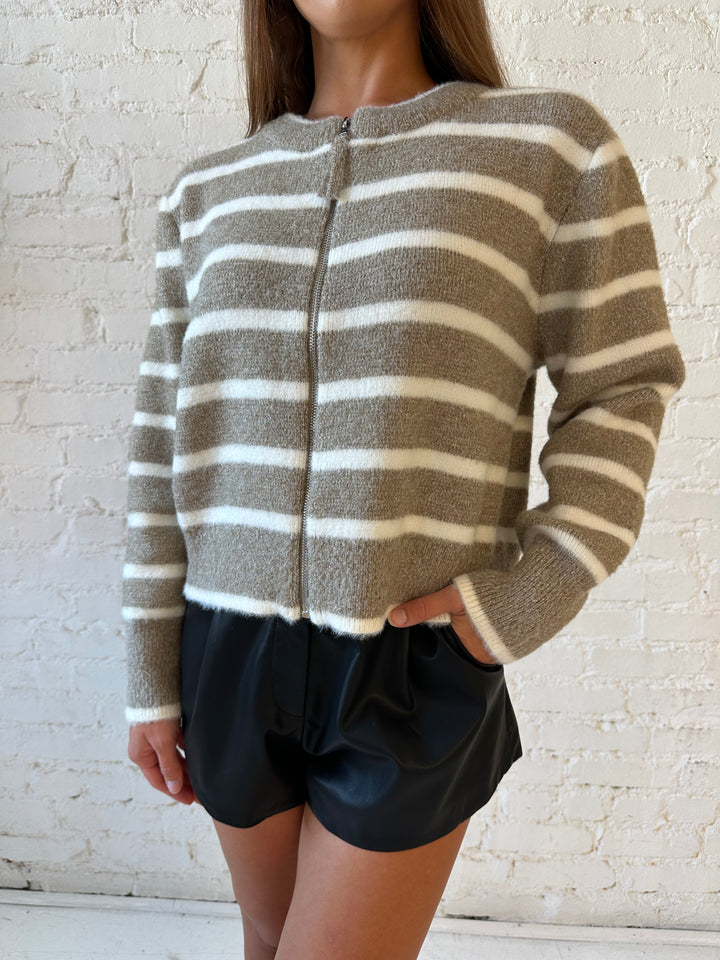 Woman wearing taupe striped zip up knit jacket with black faux leather shorts. 