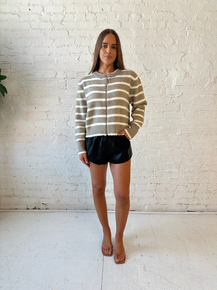 Woman wearing taupe striped zip up knit jacket with black faux leather shorts. 