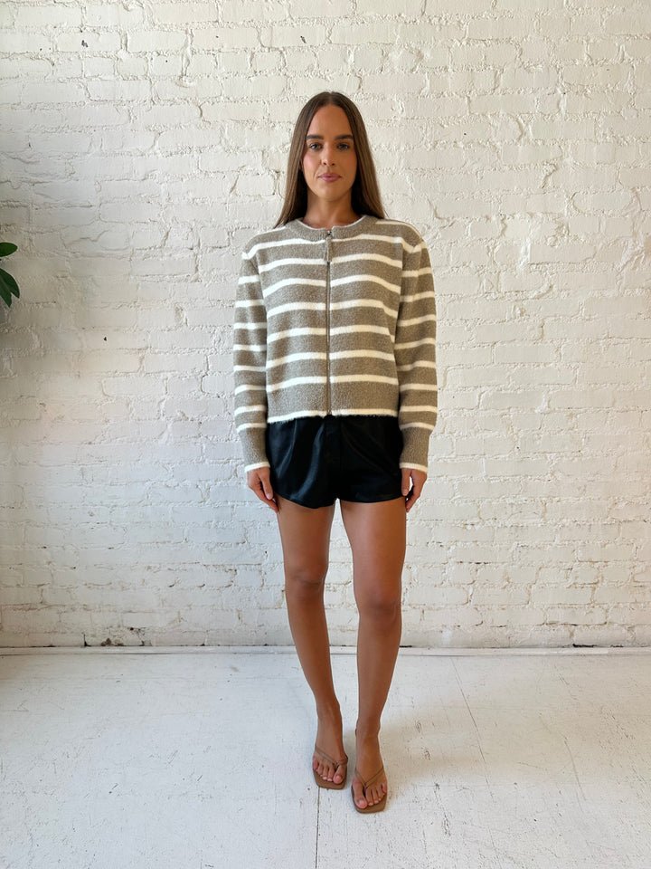 Woman wearing taupe striped zip up knit jacket with black faux leather shorts. 