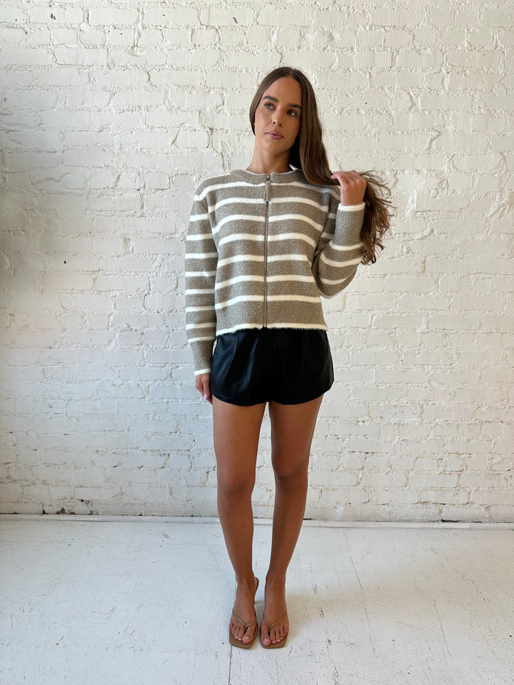 Woman wearing taupe striped zip up knit jacket with black faux leather shorts. 