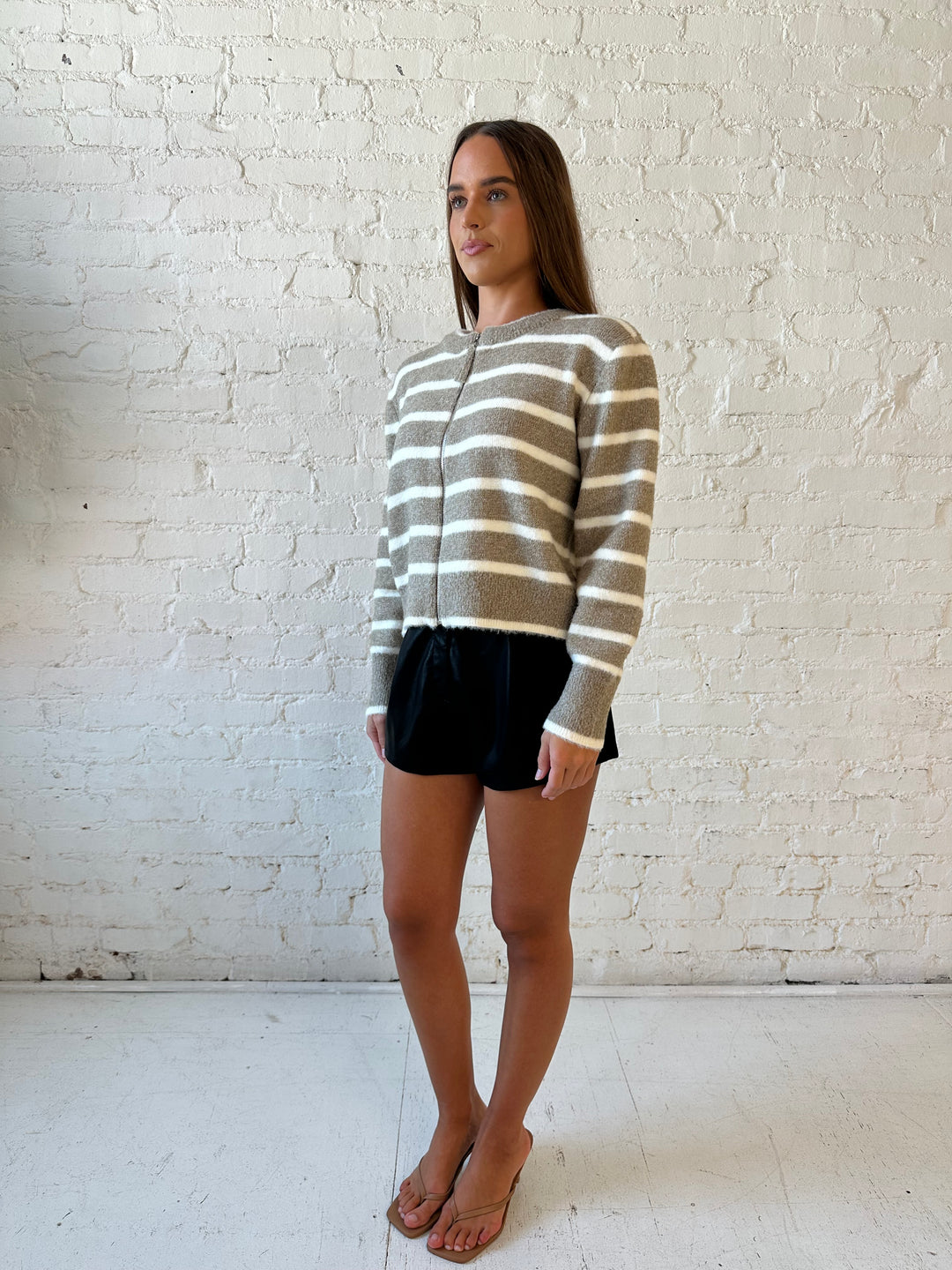 Woman wearing taupe striped zip up knit jacket with black faux leather shorts. 