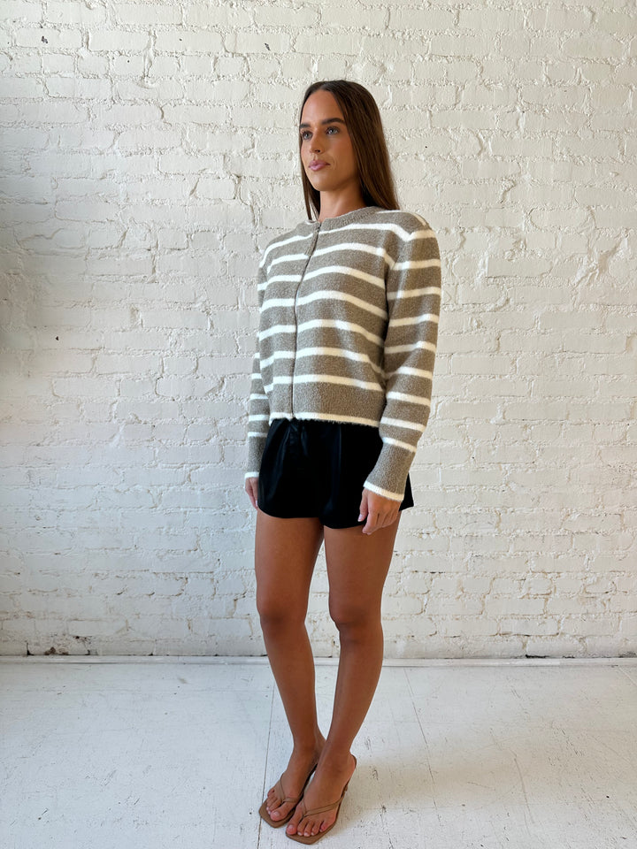 Woman wearing taupe striped zip up knit jacket with black faux leather shorts. 