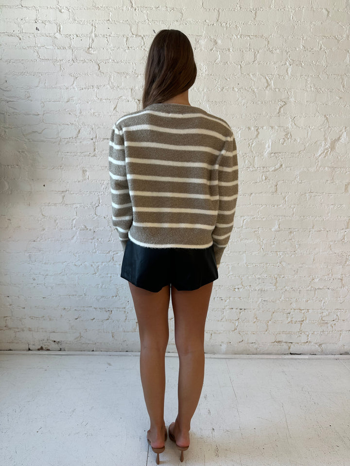 Woman wearing taupe striped zip up knit jacket with black faux leather shorts. 