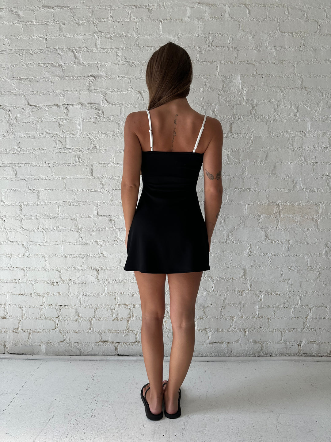 Woman wearing a black athletic mini dress with white contrast lining detail.