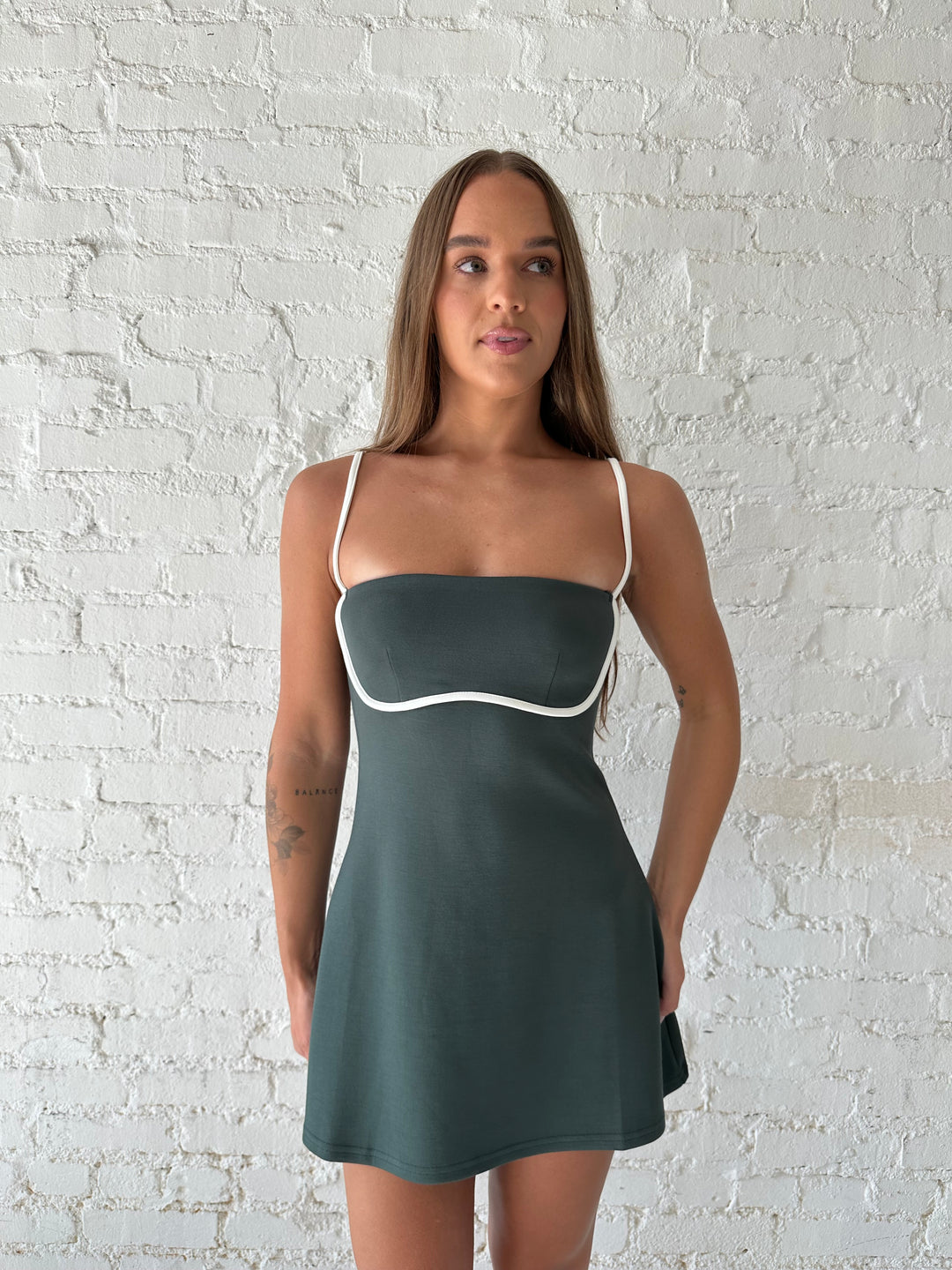 Woman wearing dark green athletic mini dress with white contrast lining detail.
