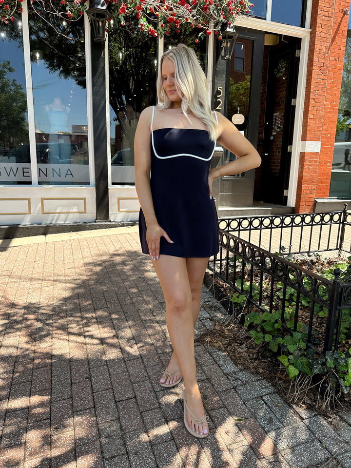 Woman wearing navy blue athletic dress with adjustable straps and built in shorts. 