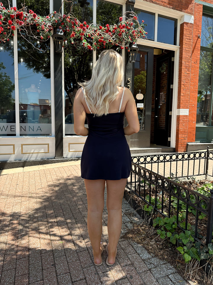 Woman wearing navy blue athletic dress with adjustable straps and built in shorts. 