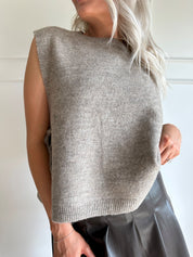 Woman wearing a brown sleeveless sweater top with tie sides and a brown pleated mini skirt.