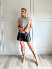 Woman wearing a brown sleeveless sweater top with tie sides and a brown pleated mini skirt.