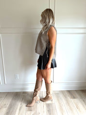 Woman wearing a brown sleeveless sweater top with tie sides and a brown pleated mini skirt.