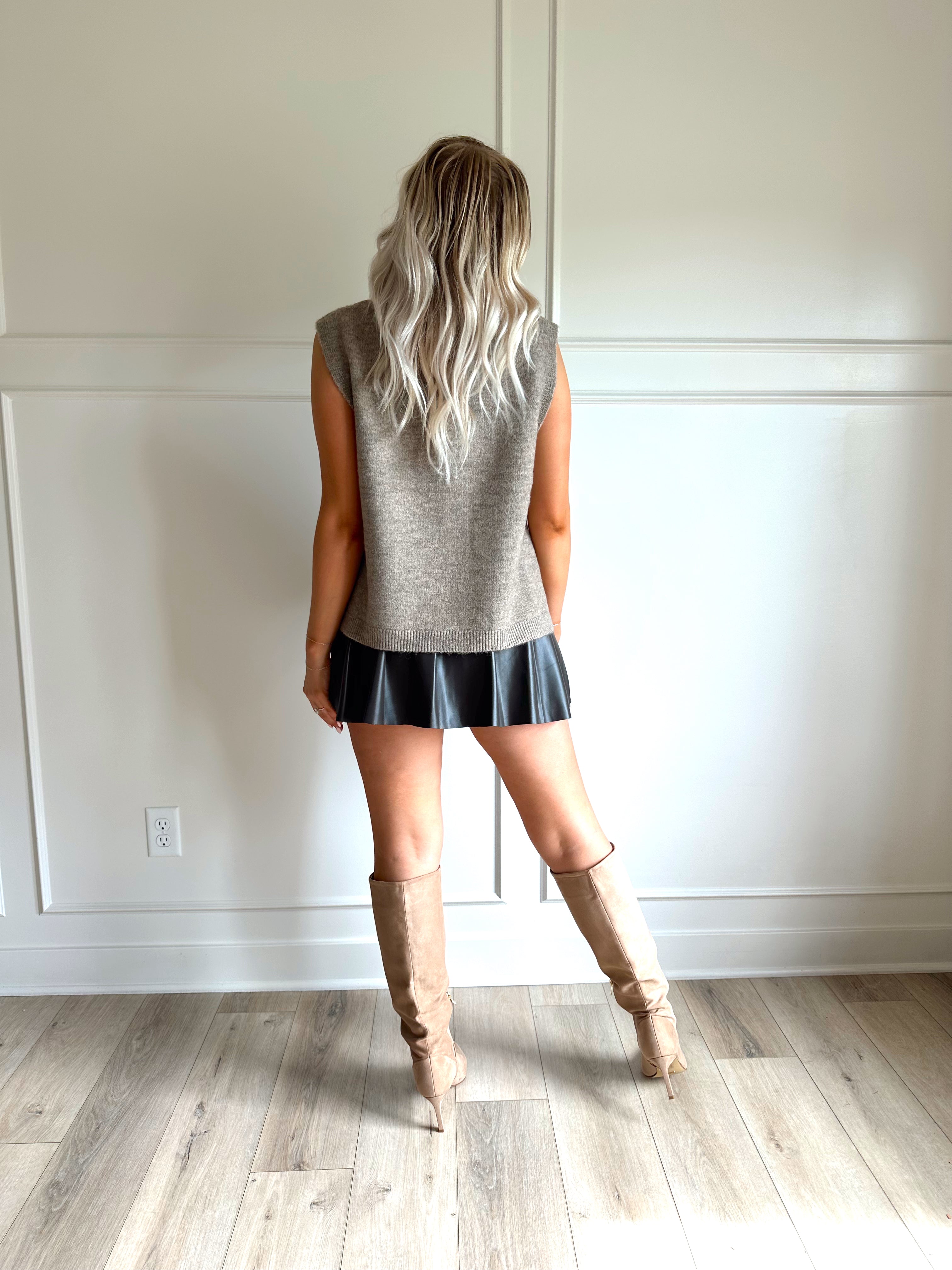 Woman wearing a brown sleeveless sweater top with tie sides and a brown pleated mini skirt.