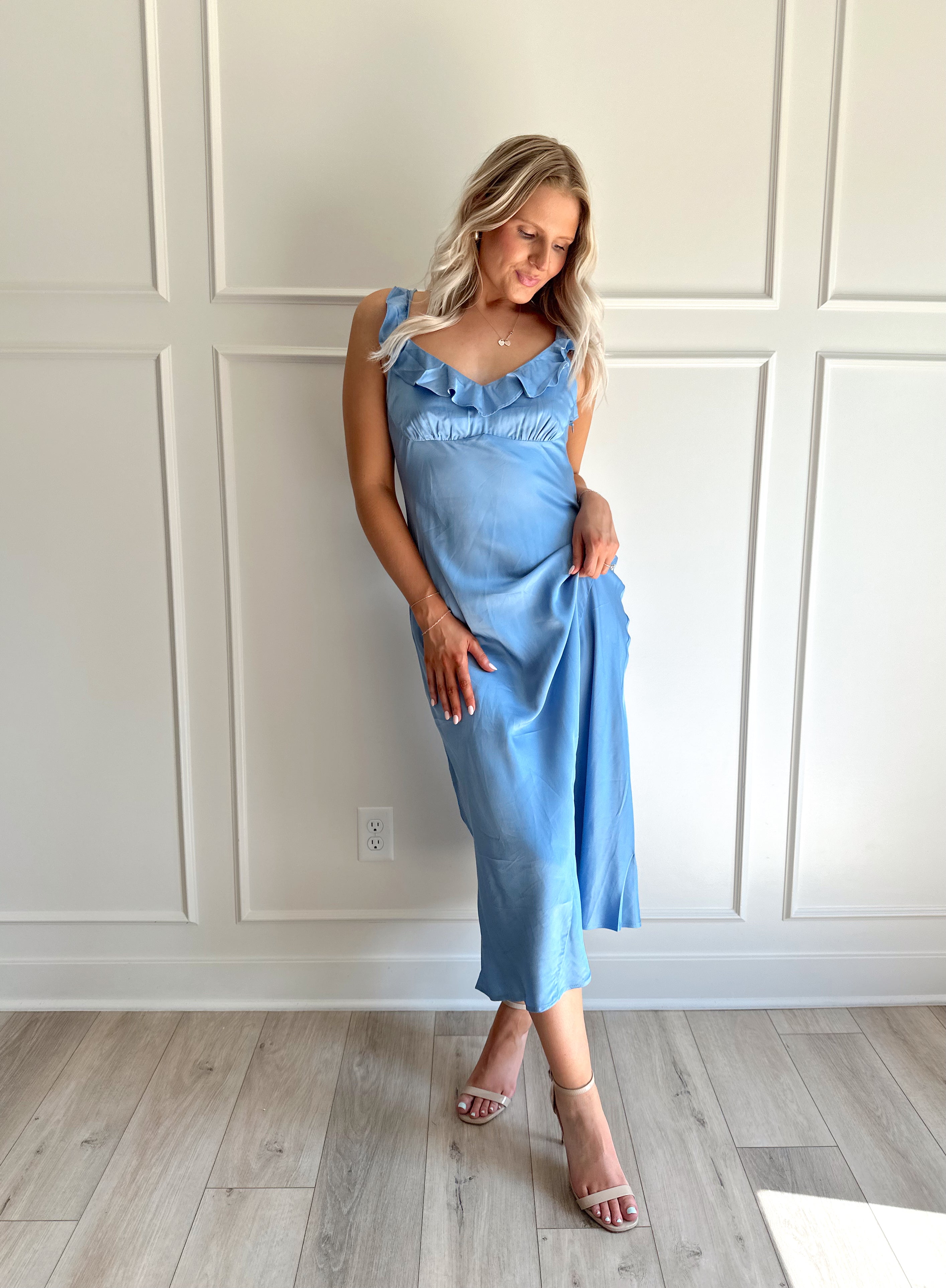 Woman wearing a light blue satin midi dress with ruffle trim along neckline. 