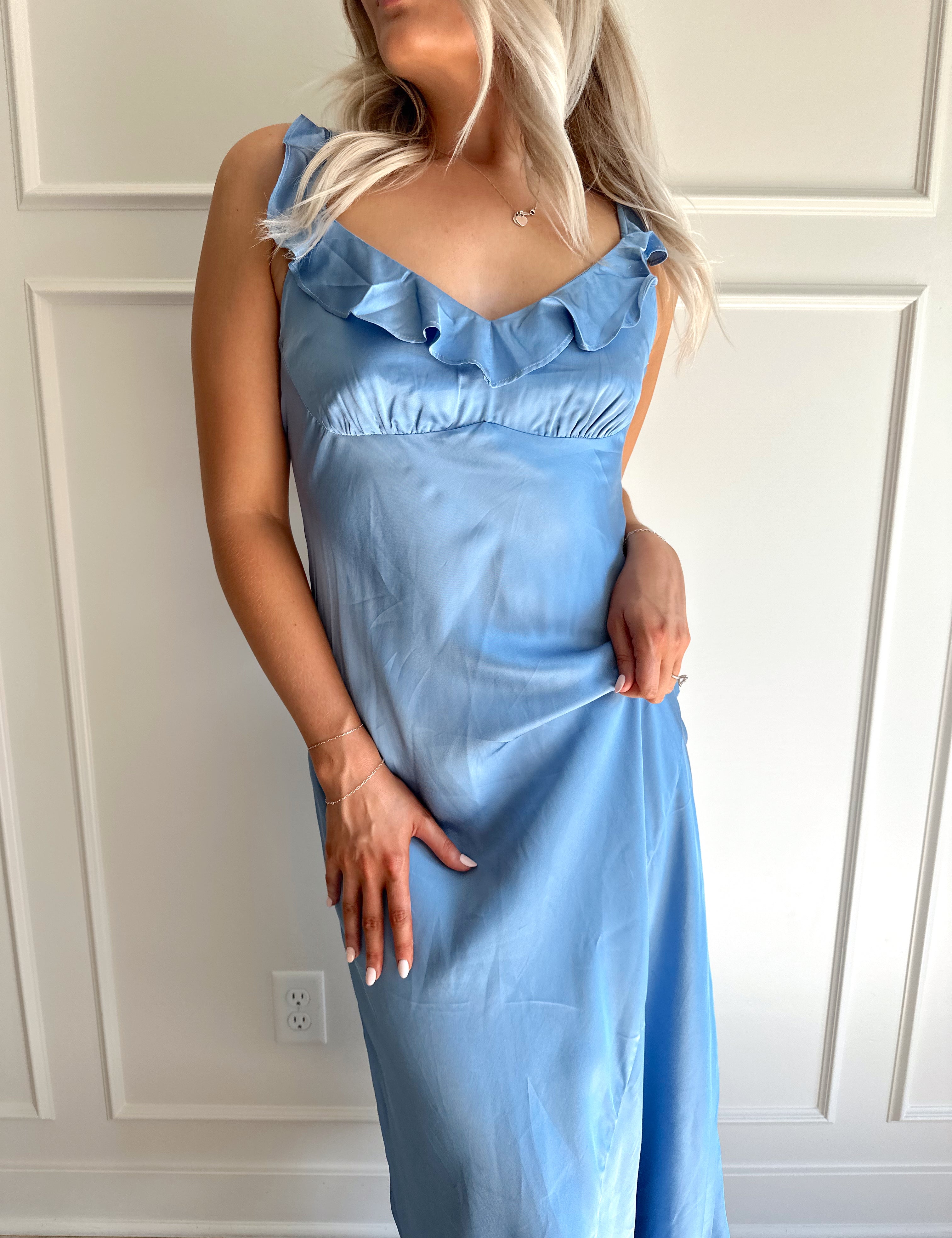 Woman wearing a light blue satin midi dress with ruffle trim along neckline. 
