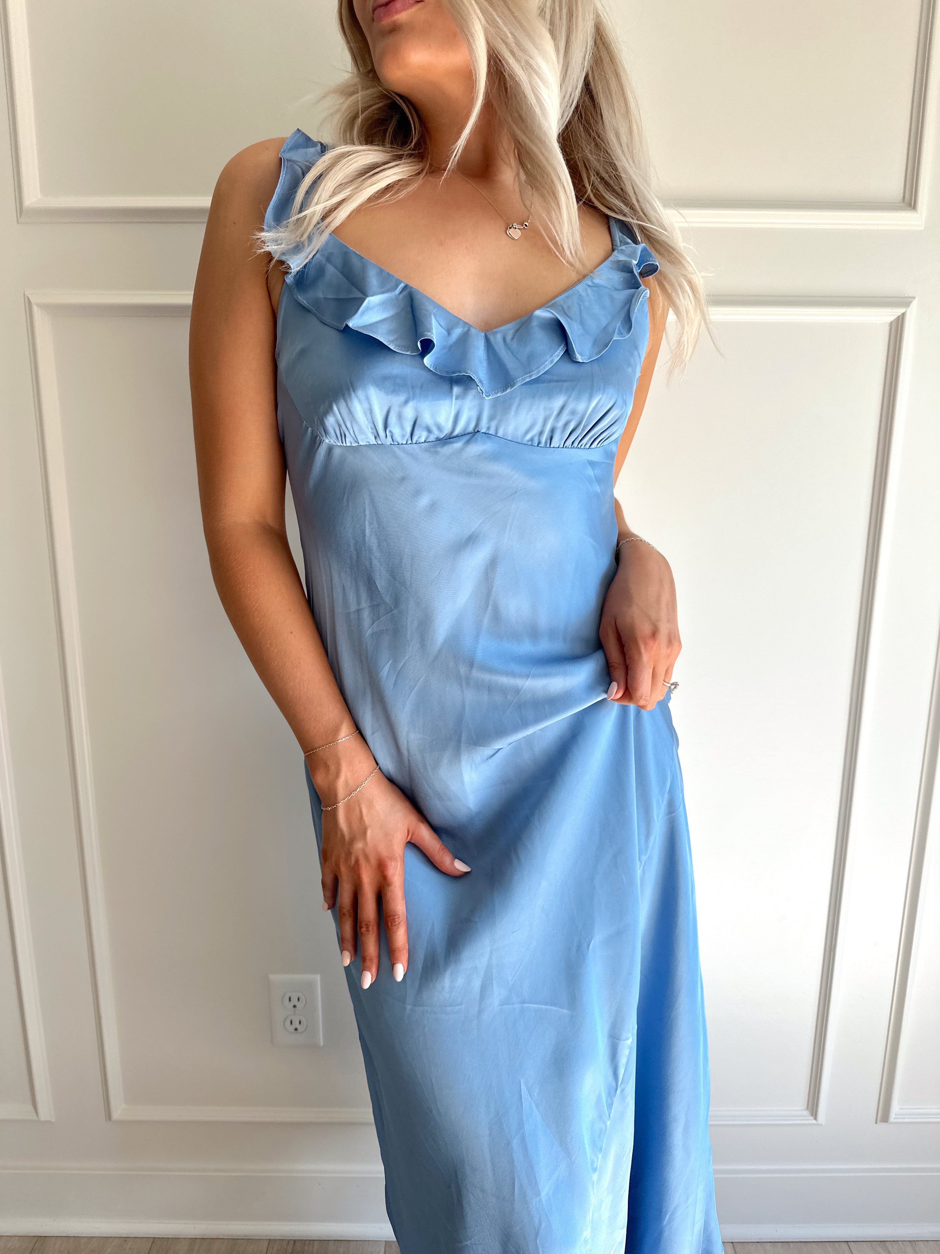 Woman wearing a light blue satin midi dress with ruffle trim along neckline. 