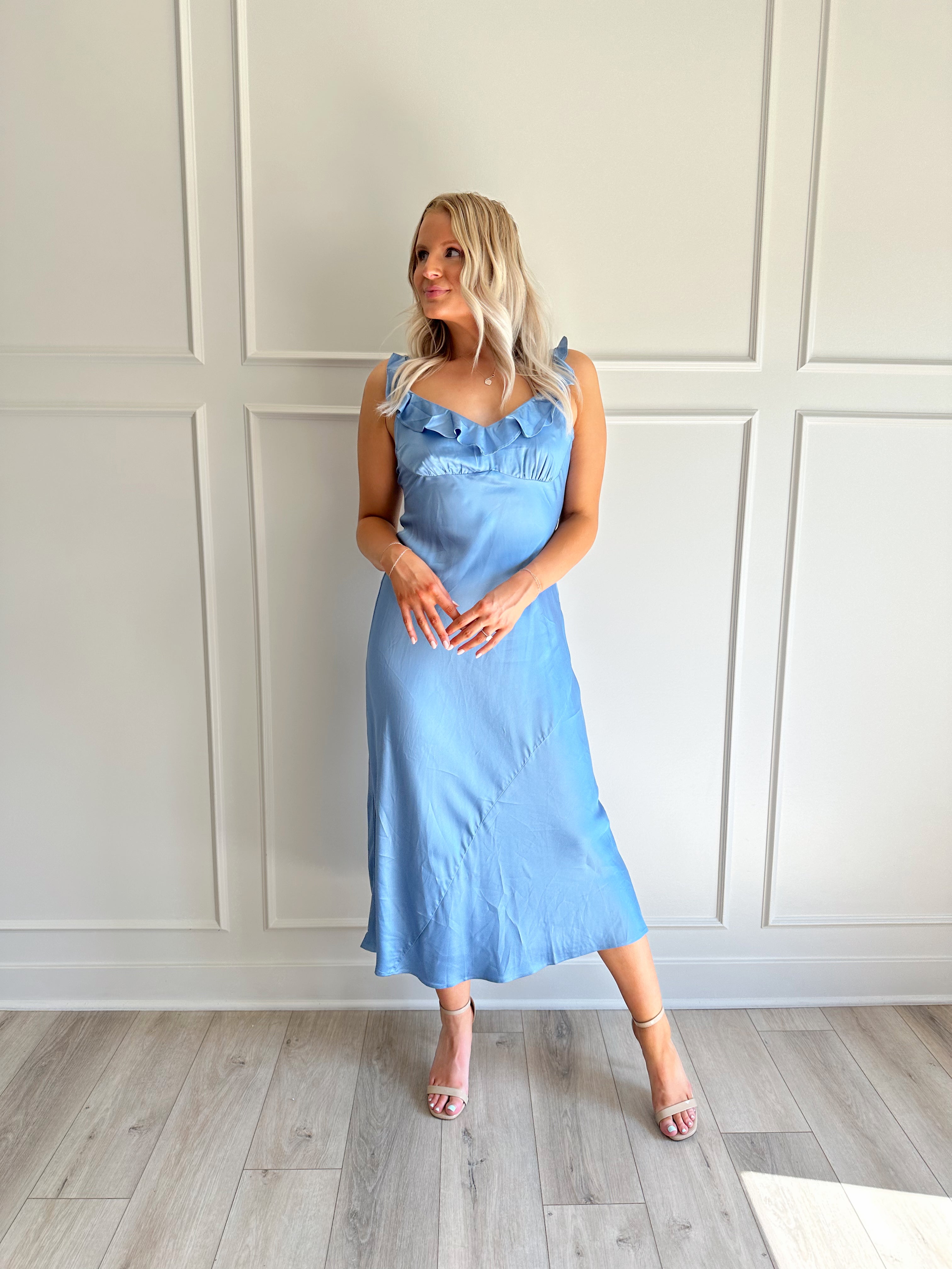 Woman wearing a light blue satin midi dress with ruffle trim along neckline. 