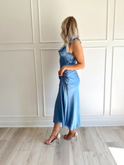 Woman wearing a light blue satin midi dress with ruffle trim along neckline. 