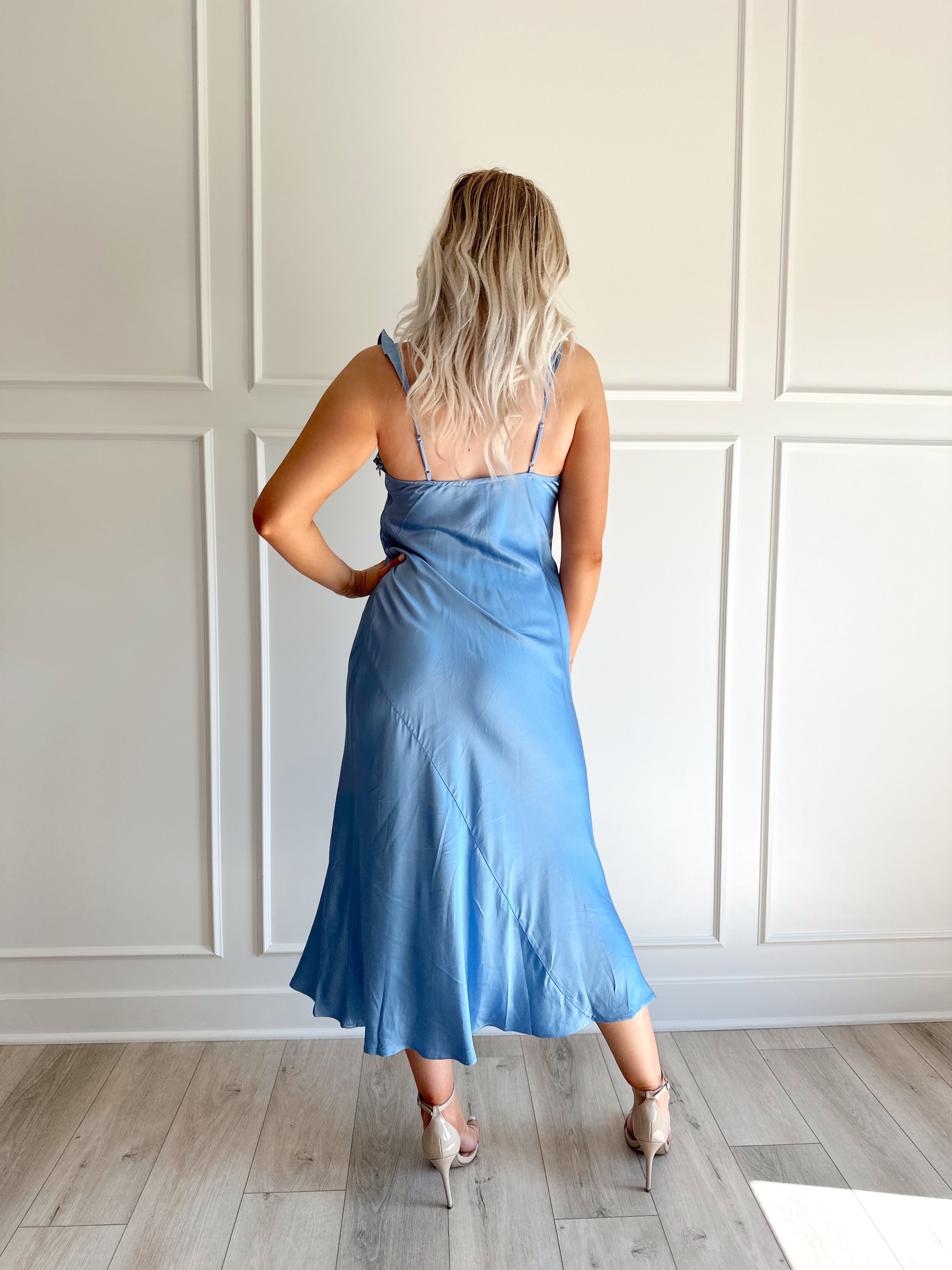 Woman wearing a light blue satin midi dress with ruffle trim along neckline. 