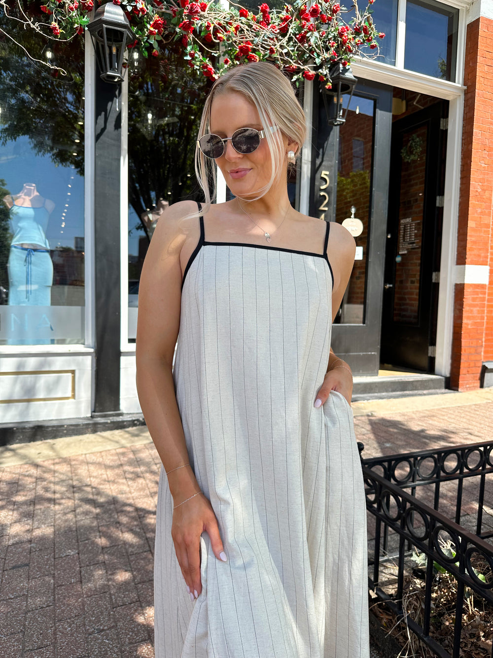 Woman wearing neutral pinstripe maxi dress, with adjustable spaghetti straps. 