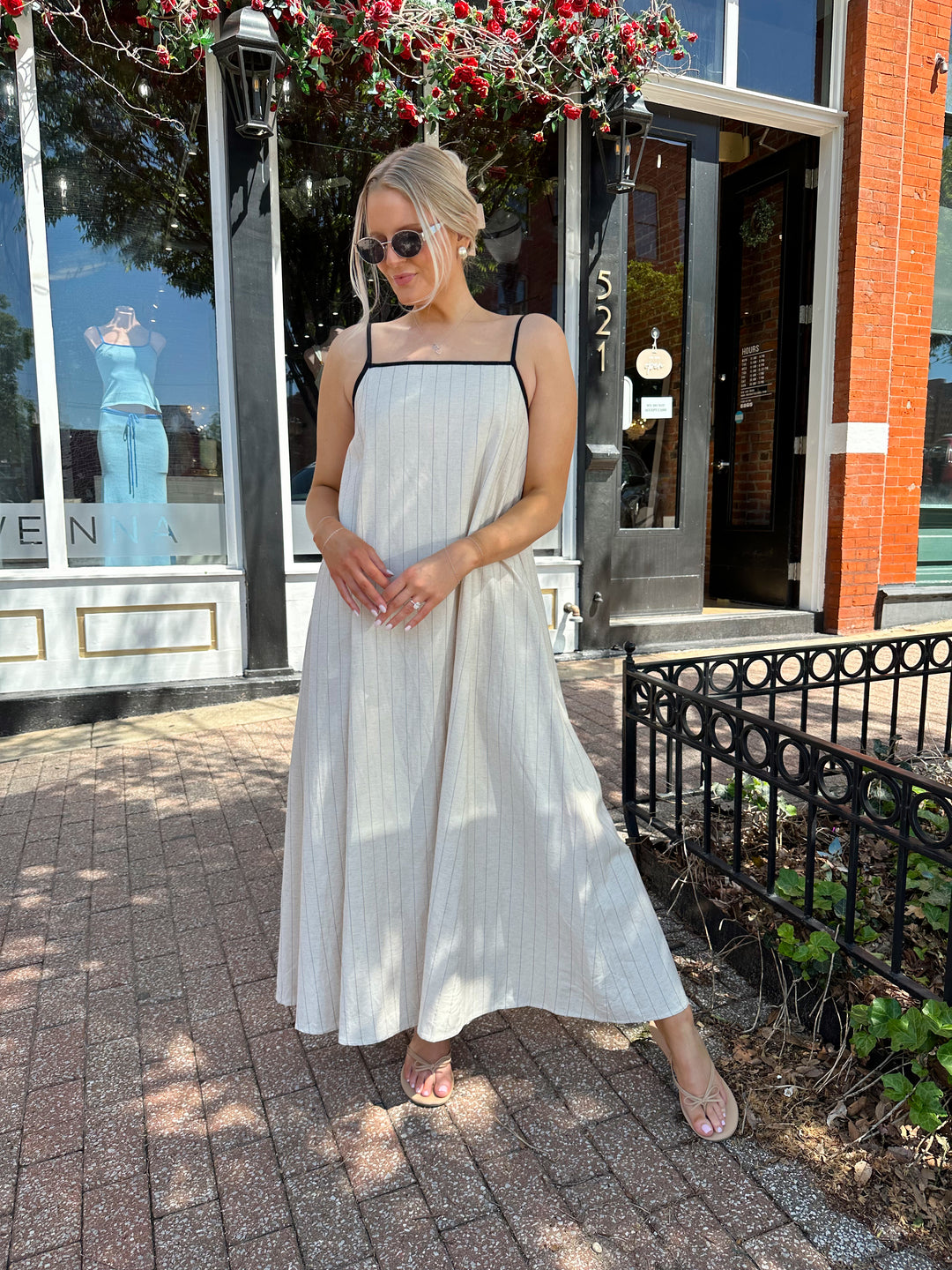 Woman wearing neutral pinstripe maxi dress, with adjustable spaghetti straps. 
