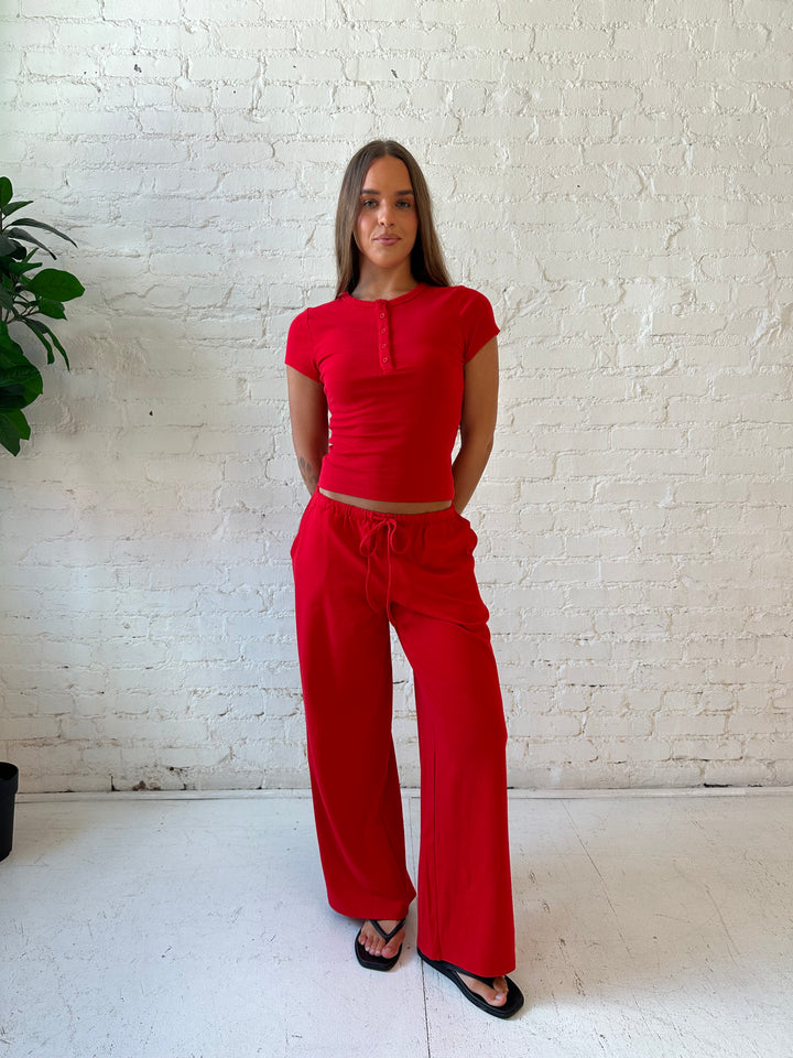 Woman wearing bright red two piece wide leg lounge set with short sleeve fitted top. 