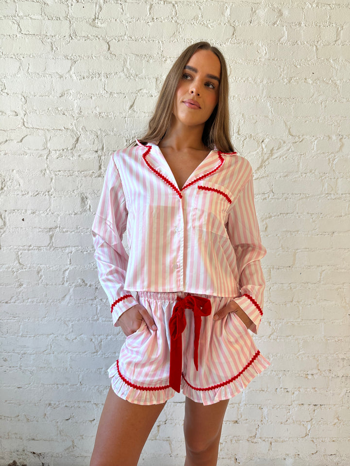 Woman wearing light pink and white striped pajamas with red trim and red Merry and Bright wording on the back. 
