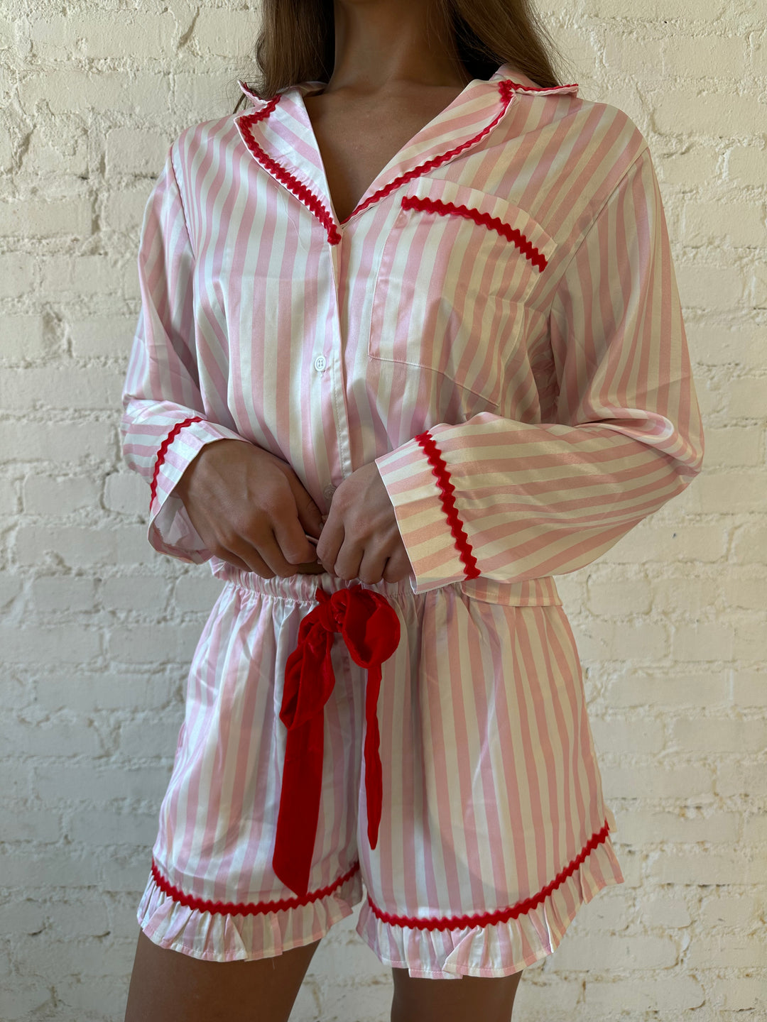 Woman wearing light pink and white striped pajamas with red trim and red Merry and Bright wording on the back. 
